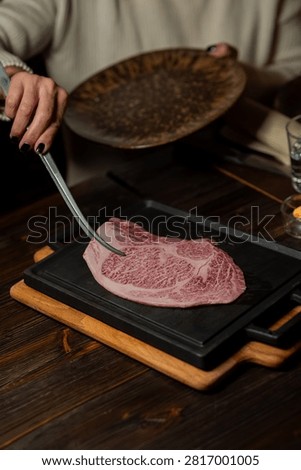 Premium beef cut, consistent with ribeye, entrecote, or sirloin, cooking on a hot cast iron plate in an elegant brasserie restaurant. Visible marbling, caramelized crust. Luxury steakhouse atmosphere, dramatic lighting. Suitable for steak restaurants, gourmet bistrot, and premium food communication.