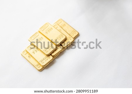 A premium macro close-up photograph capturing a collection of mini fine gold bullion bars piled neatly inside a small ceramic bowl. The image highlights the brilliant metallic shine, polished surfaces, and official weight stamp engravings on each tiny ingot. Set on a rustic dark wooden desk, the warm, dramatic lifestyle lighting accentuates the rich golden glow and contrasting textures, with a vintage leather pouch and a jeweler's magnifying loupe softly blurred in the background. Perfect for wealth management marketing, gold investment consulting, precious metals trading websites, and luxury financial stock photography