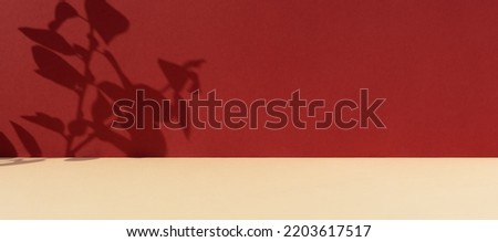 Premium podium with a shadow of plant leaves on a red wall and a beige table. Minimal abstract background for the presentation of a cosmetic product. Showcase, display case.