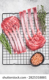 Premium raw lamb rack bone in meat on cooling rack with herbs light stone background top view culinary ingredient.