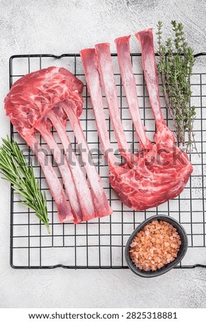 Premium raw lamb rack bone in meat on cooling rack with herbs light stone background top view culinary ingredient.
