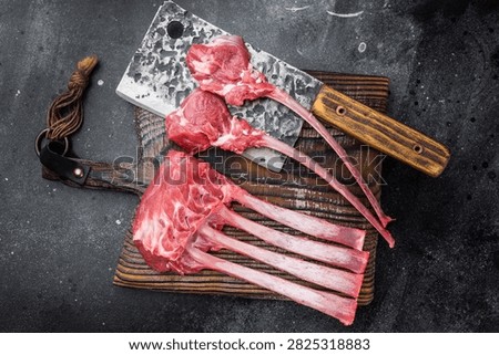 Premium raw lamb rack and sliced cutlets with bone on rustic board dark background culinary butcher style.