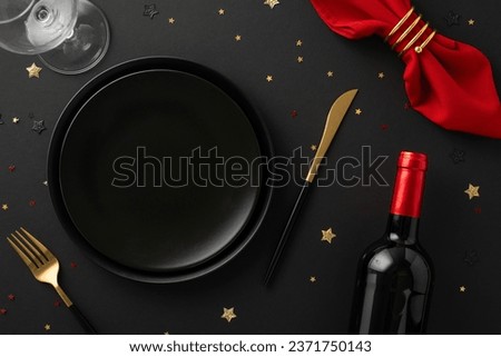 Premium restaurant New Year's special. Top view of table setup including plates, tableware, red napkin and holder, wine bottle, glass, glistening confetti against black background with space for text