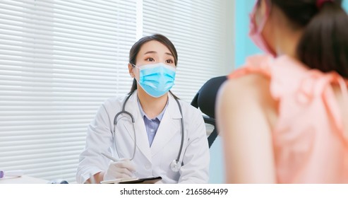 Prenatal Exam Concept - Asian Female Doctor Wearing Face Mask Is Diagnosing Pregnant Woman And She Takes Note On Paper Document In Hospital