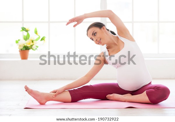 Pre-natal exercises. Beautiful pregnant\
woman exercising while sitting in lotus position\
