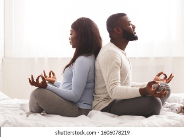 Prenatal yoga. Expecting black woman doing yoga with her husband at home, sitting on back to back with closed eyes