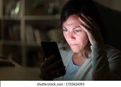 Preoccupied adult woman reading on smart phone lighted screen sitting at night at home - Powered by Shutterstock