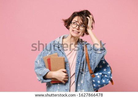 Preoccupied woman student in denim clothes eyeglasses backpack isolated on pastel pink background. Education in high school university college concept. Mock up copy space. Hold books put hand on head
