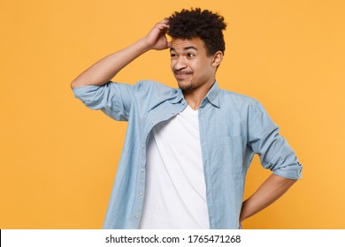 Preoccupied young african american guy in casual blue shirt posing isolated on yellow wall background studio portrait. People lifestyle concept. Mock up copy space. Put hand on head, looking aside