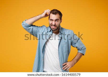 Preoccupied young bearded man in casual blue shirt posing isolated on yellow orange background studio portrait. People emotions lifestyle concept. Mock up copy space. Putting hand on head, looking up