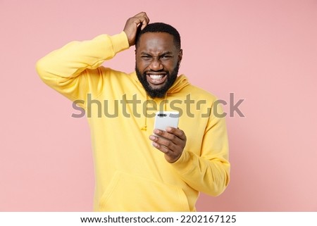 Preoccupied young man 20s wearing casual yellow streetwear hoodie using mobile cell phone typing sms message put hand on head isolated on plain light pastel pink color background studio portrait