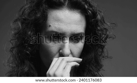 Preoccupied young woman biting nails feeling overwhelmed with problems. person struggling with crippling anxiety captured in intense dramatic monochromatic black and white
