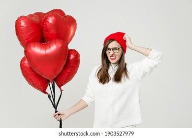 Preoccupied young woman in sweater red hat glasses put hand on head celebrating birthday holiday party hold bunch of heart air inflated helium balloons isolated on white background studio portrait
