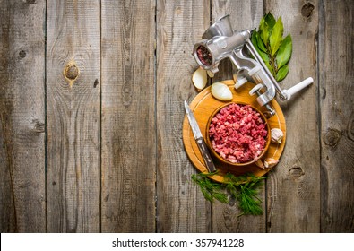 Preparated minced meat in a bowl , grinder and spices with herbs. On a wooden table. Free space for text . Top view