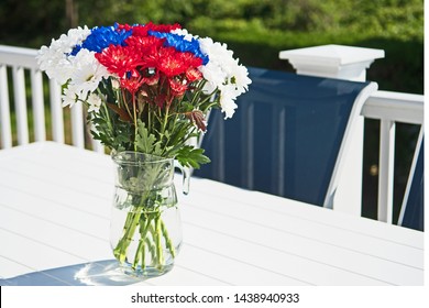 In Preparation For The 4th July Celebration, A Beautiful Bouquet Of Red, White And Blue Flowers Is The Centerpiece Of An Outside Table.