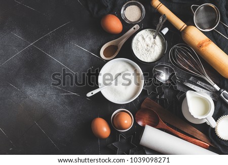 Preparation baking kitchen ingredients for cooking. Grocery accessories for home pastry eggs flour sugar yeast milk spoon whisk for cooking food on dark background with copy space flat lay top view