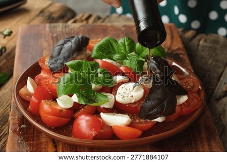 Preparation of caprese salad. Adding olive oil to salad made of chopped tomatoes, mozzarella and basil. Italian cuisine.