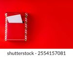 Preparation for Christmas celebration concept. Writing letter to Santa Claus tradition. Miniature red striped mailbox with letters, envelopes and Christmas decorations on red background 