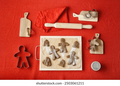 Preparation Cooking ginger cookies, Christmas and New Year traditional cookies in shape of gingerbread mans and bells, metal pastry cutter on dough, wooden rolling pin on red linen tablecloth, above - Powered by Shutterstock