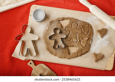 Preparation Cooking ginger cookies, Christmas and New Year traditional cookies in shape of gingerbread mans and bells, metal pastry cutter on dough, wooden rolling pin on red linen tablecloth, above - Powered by Shutterstock