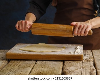 Preparation of dough products by a professional chef in a professional kitchen. The chef rolls out the dough on a wooden cutting board with a rolling pin. Bakery, restaurant, hotel, cafe, pastry shop.