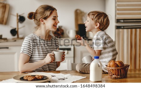 preparation of a family breakfast. mother and child son cut bread and eat cookies with milk in morning
