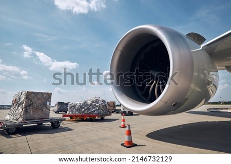 Preparation freight airplane at airport. Loading of cargo containers against jet engine of plane.
