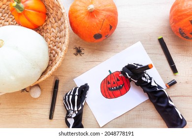Preparation for the holiday Halloween  Hands in black gloves and bones are drawing sketch and markers laughing pumpkin  wooden desk surrounded by pumpkins   spiders  top view 