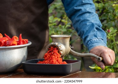 Preparation Of Homemade Sauce With A Sweet Bell Peppers, Hot Pepper Chilli With A Grinding Machine. Man Grinding Red Peppers On Old Meat Grinder Outdoors Close-up. Vegetable Sauce Healthy Organic Food