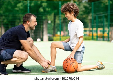 Preparation. Portrait of supportive man tying shoelaces of curly boy on basketball playground, blurred background - Powered by Shutterstock