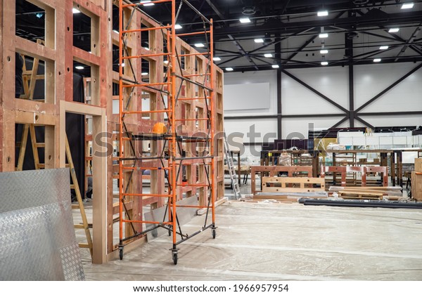 Preparation of the premises for the\
exhibition. Installation of partitions in the exhibition hall.\
Scaffolding next to a wooden frame in the exhibition complex.\
Installation of advertising\
structures.