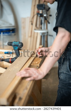Preparation process in restoration workshop, man crafter working with wooden details and materials, craftsperson selecting and making marks on plank for window frame, handwork and reconstruction.