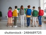 Preparation for school. Junior high school students show off their large, roomy, colorful and fashionable backpacks. Children stand in row with their backs to camera with school bags on shoulders.