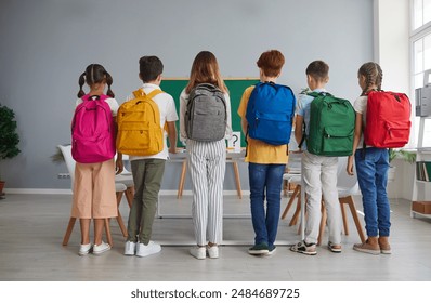 Preparation for school. Junior high school students show off their large, roomy, colorful and fashionable backpacks. Children stand in row with their backs to camera with school bags on shoulders.