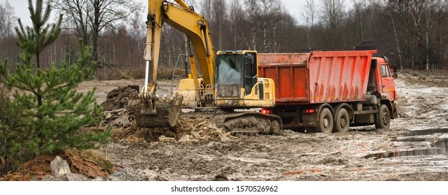 Preparation Of The Site For Construction, Leveling The Soil. Excavator Loads Excess Soil Into Dump Trucks