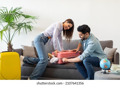 Preparation for vacation. Happy spouses packing and trying to close suitcase on sofa, preparing for travel at home. Vacation, family travel together and positive emotions - Shutterstock ID 2107641356