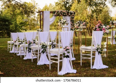 Preparation for a wedding ceremony outdoor in the park/ forest . Wood arch and chairs are decorated with white and pink flowers roses and peony, on the ground are many wood lanterns with candles.  