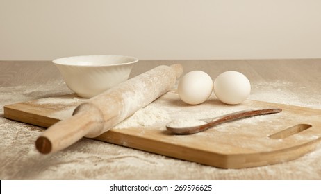 Preparations for homemade baking. Basic ingredients for baking. Kitchen utensil with eggs rolling-pin wood spoon meal. Meal on table with cutting board. Flour. baking