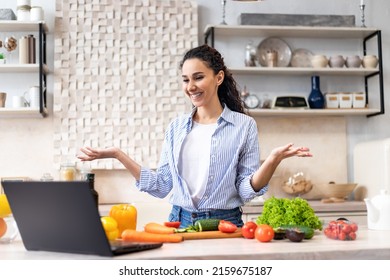 Prepare Food At Home. Happy Latin Lady Cooking And Talking On Video Chat With Family Via Laptop Computer, Preparing Salad In Light Kitchen, Copy Space