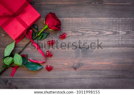 Prepare the prsesnts or surprise for Valentine's day. Red gift box near red rose on dark wooden background top view space for text