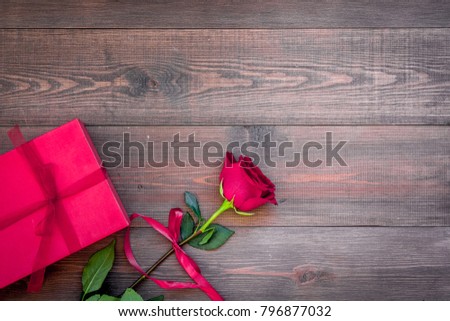 Prepare the prsesnts or surprise for Valentine's day. Red gift box near red rose on dark wooden background top view space for text