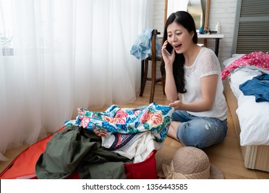 Prepare For Travel. Happy Asian Woman Talking On Mobile Phone Sitting On Floor With Suitcase Nearby. Young College Girl Student Going On Field Trip Chatting On Cellphone With Classmate While Packing.