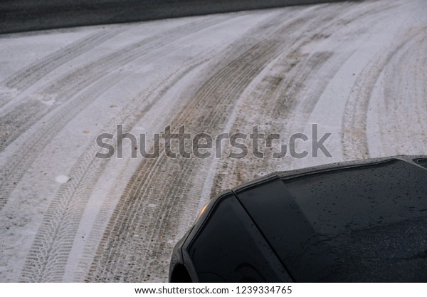 Prepare your car for winter driving by choosing right\
winter tires. Dark blue car driving on light snow with visible tire\
marks. 