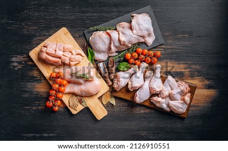 Prepared for frying, butchered various portions of raw chicken meat. Set of raw chicken fillet, thigh, wings, strips and legs on the background of the culinary table with spices and cherry tomatoes