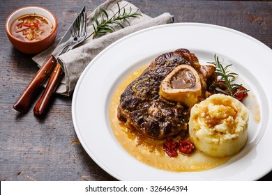 Prepared Osso buco Veal shank with tomatoes and mashed potatoes on white plate on wooden background
