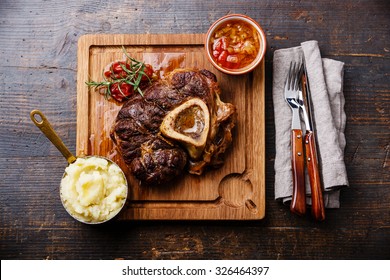 Prepared Osso buco Veal shank with tomatoes and mashed potatoes on serving board on wooden background