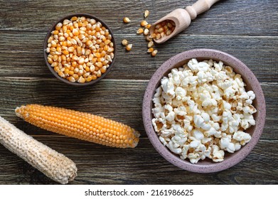 Prepared popcorn in bowl, corn seeds and corncobs on wooden background. The top view