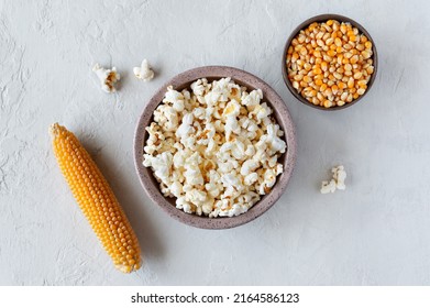 Prepared popcorn in bowl, corn seeds and corncobs on concrete background. The top view