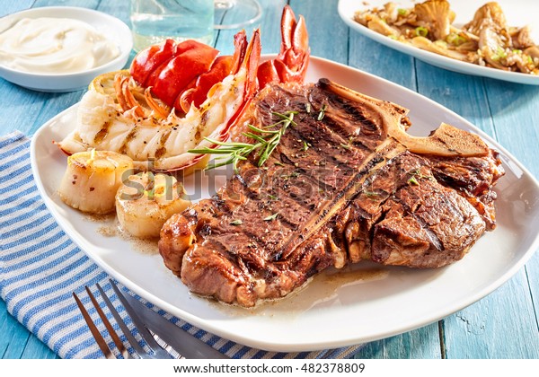 Prepared surf and turf well done steak and lobster\
meal with side dishes of crab cakes, shrimp and mayonnaise dip on\
blue wooden table