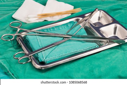 Prepares wound suture tray materials for use at the emergency room.cotton but gauze, tooth and non tooth forceps , green cover pad mayo scissors in silver tray. select focus.